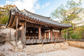 Obraz premium Traditional Korean Hanok Building Featuring Wooden Porch, Detailed Eaves, and Stone Wall with Forest Background