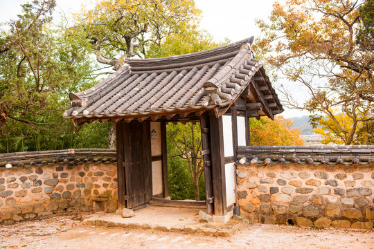 raditional Korean Hanok Entrance Gate Featuring Stone Wall and Tiled Roof Surrounded by Forest and Autumn Foliage