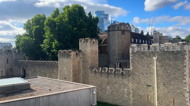Historic fortified stone walls and towers stand beneath scattered clouds as a modern skyline rises behind them