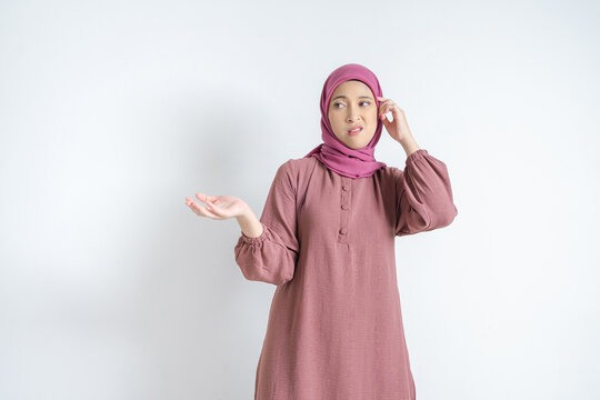 Confused Asian Muslim woman in hijab scratching head with puzzled expression on white background