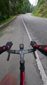Vertical POV footage of a cyclist riding on a winding mountain road through tropical forest with another cyclist ahead, capturing outdoor adventure, fitness and scenic travel.