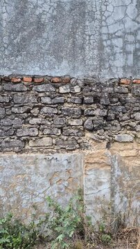 ​Textured old wall with layers of natural stone, red bricks, and cracked concrete plaster in daylight