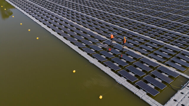 An aerial view shows workers cleaning solar panels in a large body of water.