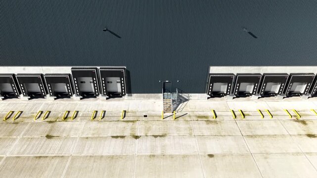 Dynamic low-pass aerial view sweeping along the industrial concrete aprons and shutter doors of a warehouse distribution centre.