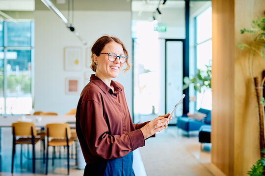 Happy business woman using a digital tablet, standing at a contemporary workplace, portraying success and entrepreneurship
