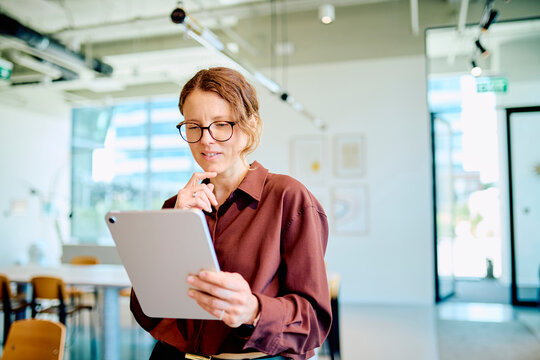 Businesswoman thinking and analyzing information on a digital tablet, working efficiently in a modern bright office environment