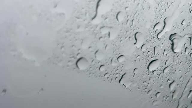 Close up of water droplets sliding down a window pane during a rainy day. Cinematic minimalist background for mood and weather concepts.
