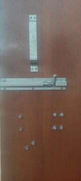 Close up view of a brown wooden door featuring a silver handle and a sturdy sliding bolt latch