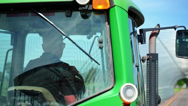 Farmer operating a agricultural tractor going through greenhouse. Close up shoot of modern farming equipment used for fieldwork and crop production.