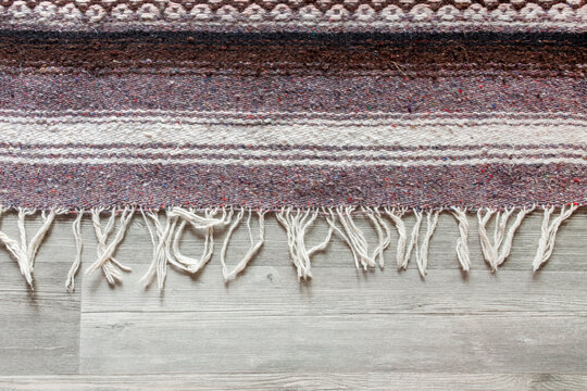 Handmade woven rough pile purple patterned scatter rug on a grey laminate floor background backdrop. Modern home decor concept.