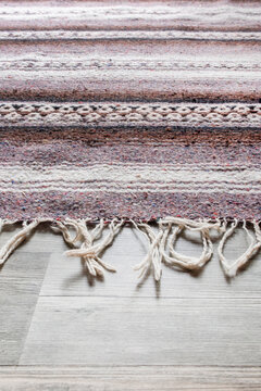Handmade woven rough pile purple patterned scatter rug on a grey laminate floor background backdrop. Modern home decor concept.