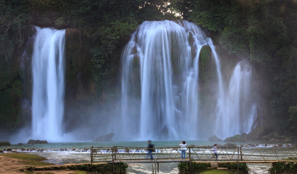 Majestic Ban Gioc waterfall with tourists walking on bamboo bridge in Cao Bang, northern Vietnam⁠
