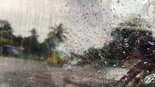 View through a wet windshield during a downpour, with blurred traffic and water droplets creating a moody driving scene and reduced visibility