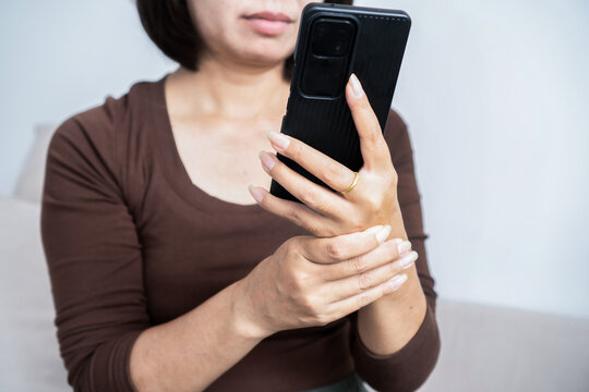Woman holding wrist feeling pain and numbness from using smartphone. Asian female suffering from wrist injury, carpal tunnel syndrome, tendonitis, or muscle fatigue from phone addiction
