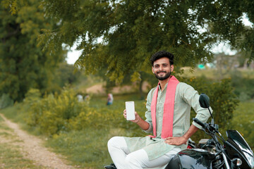 Fototapeta premium Young indian farmer showing smartphone screen while sitting on motorbike