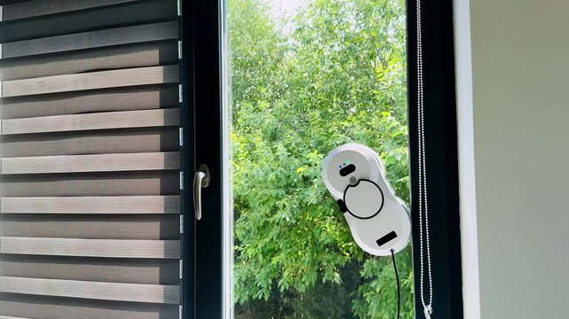 Robot window cleaner firmly attached to a glass surface surrounded by leafy greenery
