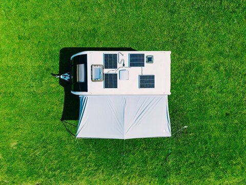 Solar panel array mounted on RV roof with awning set up on a vibrant green grassy field