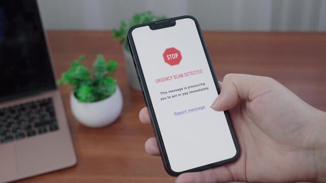 Person checks an AI information message flagging an urgency scam on a phone at a wooden desk.