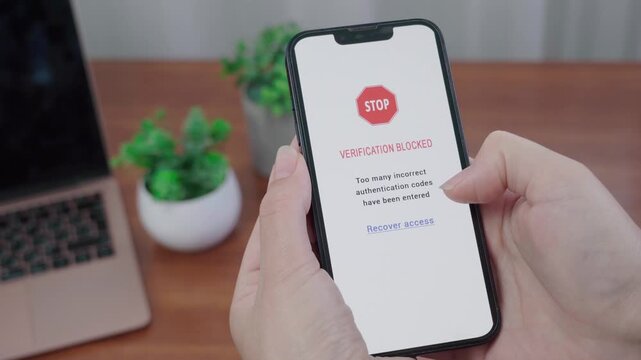 User holds a phone displaying an AI verification blocked message after too many incorrect authentication codes with a recover access link.