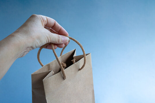 Hand holding a brown color paper shopping bag. Against blue background.