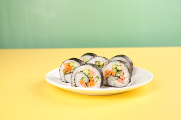 Vegetable sushi rolls on white plate with yellow table and green background © TrinhVan