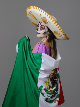 Day of the Dead woman in sombrero wrapped in Mexican flag on gray background