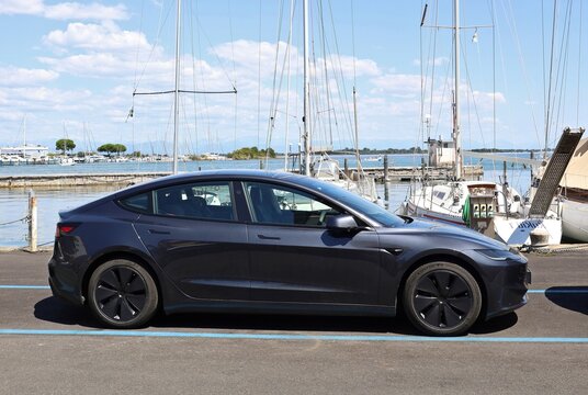 Grado, Italy. July 22, 2026. Black Tesla Model 3, new version known as Highland, parked by a marina pier