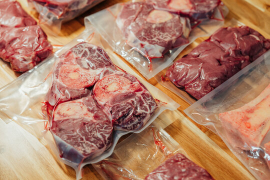 Close-up of vacuum sealed raw beef shanks, marrow bones, and organ meat arranged on a wooden surface for storage and cooking