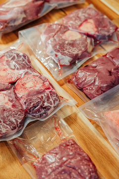 Close-up of vacuum sealed raw beef shanks, marrow bones, and organ meat arranged on a wooden surface for storage and cooking