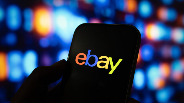 Close up hand holding smartphone displaying ebay logo with colorful blurred abstract bokeh background.