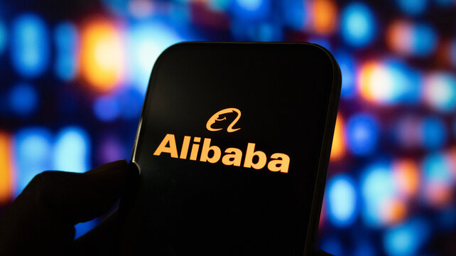 Alibaba logo on smartphone screen held by hand, bokeh lights background.
