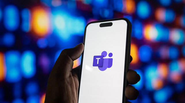 Microsoft teams application logo on mobile phone screen with hand holding device in low light set.