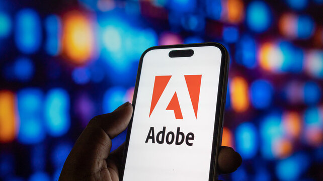 Adobe logo on smartphone screen held by hand against blurred colorful digital background abstract.