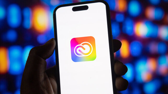 Close up of person hand holding smartphone with adobe creative cloud app icon on screen display.