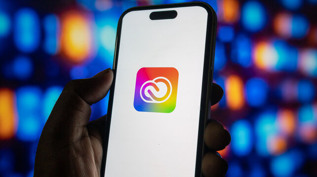 Close up of person hand holding smartphone with adobe creative cloud app icon on screen display.
