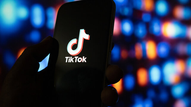 Close up of hand holding a smartphone showing the tiktok logo on screen against digital blue light.
