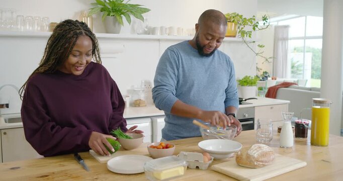 African couple cooking at kitchen island, man cracking eggs in glass bowl as woman slicing avocado
