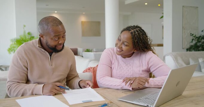 Couple sitting at table, man pointing line and signing forms with blue pen, finalizing paperwork