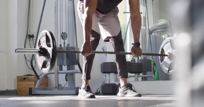 Mid-adult African man adjusting grip on loaded barbell deadlifting for strength in black-top at gym