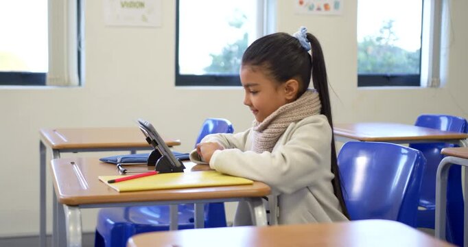African American teen focusing on tablet, leaning and tapping at school desk, completing classwork