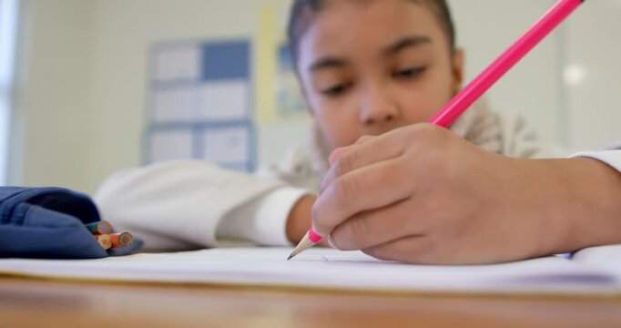 African American child holding pink pencil at desk, writing, pausing and glancing toward chart
