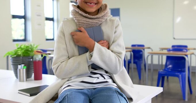 Camera pulling back African American child sitting on table in class holding book smiling at camera