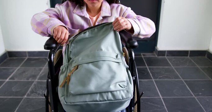 African youth in wheelchair grasping zipper pulls, unzipping backpack in entryway and accessing bag