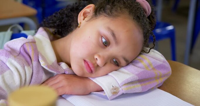 African American child lowering gaze resting head at school desk with notebook in pink top dozing