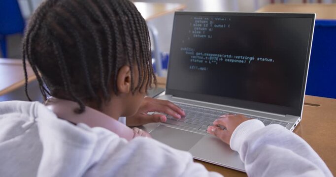 African American youth reading laptop terminal at school desk, then typing code and completing task