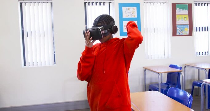 Teen wearing red hoodie picking up VR headset with headphones in class adjusting strap for lesson
