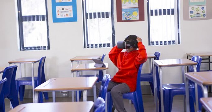 African male youth in classroom lifting VR headset testing VR glancing at tablet, copy space
