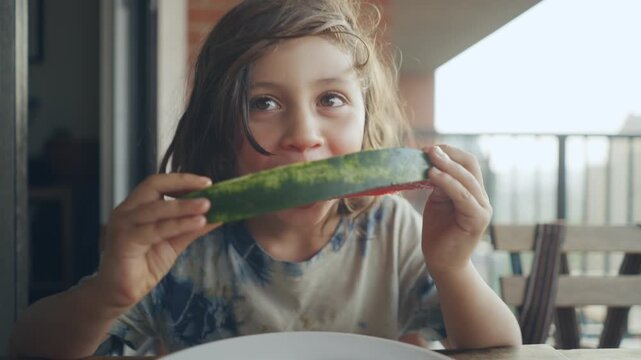 Happy child taking a big bite of watermelon on a balcony