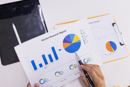 A close-up of business professionals analyzing market research reports and sales performance data using colorful charts, graphs, and a pen for pointing.
