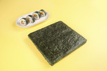 Dried seaweed sheet and vegetable sushi rolls on yellow background © LyVan